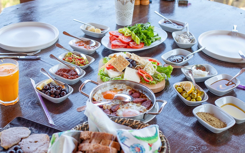 Turkish breakfast with eggs, olives, cheese, and vegetables on a wooden table.