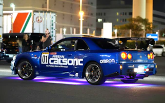 Nissan Skyline R34 at Daikoku PA car meeting, neon lights underneath.