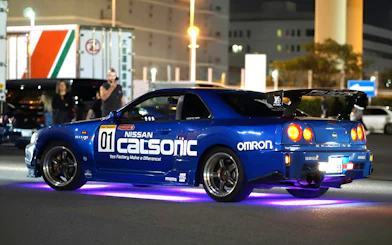 Nissan Skyline R34 at Daikoku PA car meeting, neon lights underneath.