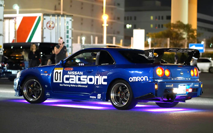 Nissan Skyline R34 at Daikoku PA car meeting, neon lights underneath.