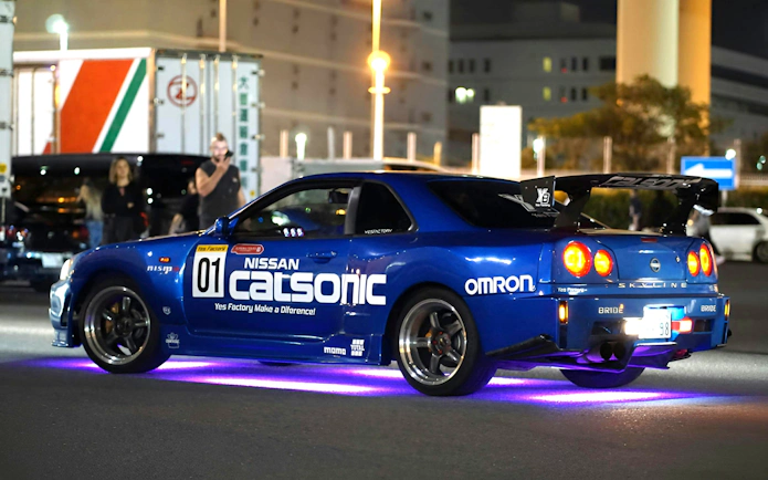 Nissan Skyline R34 at Daikoku PA car meeting, neon lights underneath.