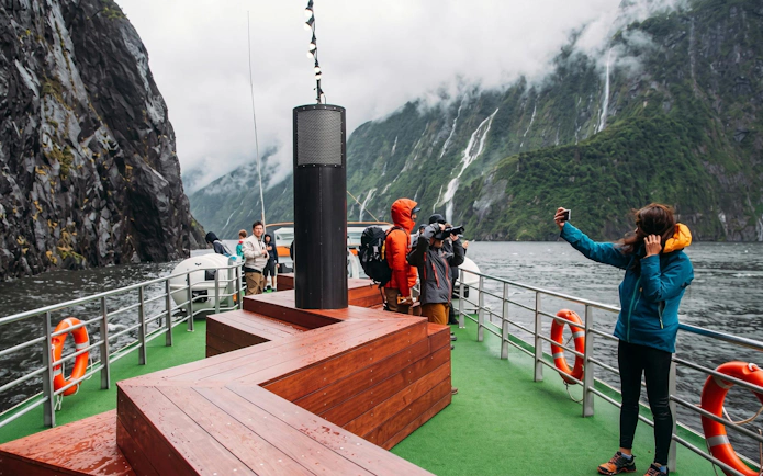 Tourists on a boat in Milford Sound, surrounded by cliffs and waterfalls, Te Anau departure.