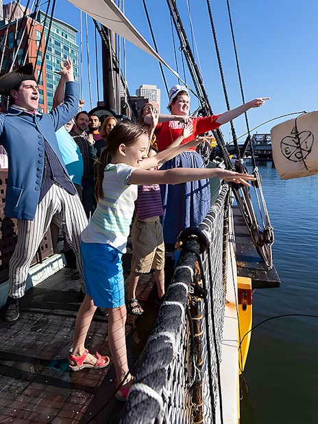 Tourists reenact Boston Tea Party by throwing tea chest from ship into harbor.