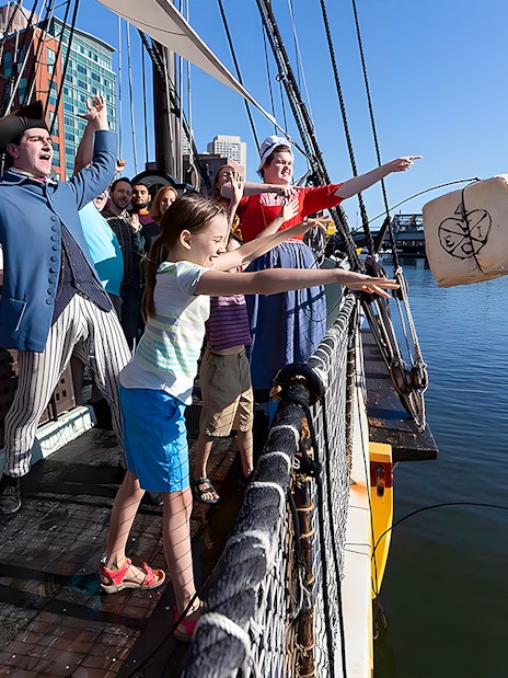 Tourists reenact Boston Tea Party by throwing tea chest from ship into harbor.