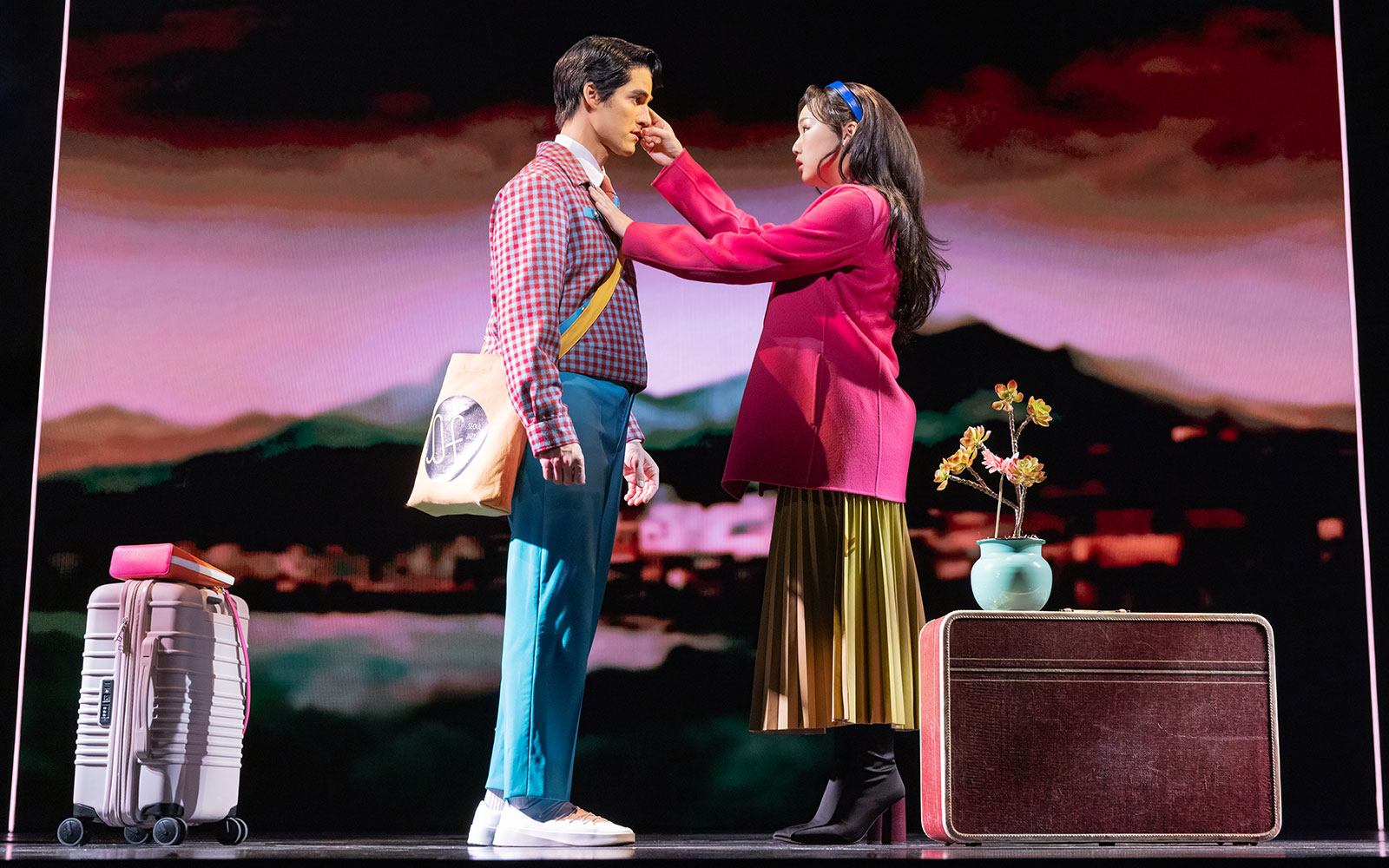 Actors performing Maybe Happy Ending Broadway show on stage with luggage and flowers.