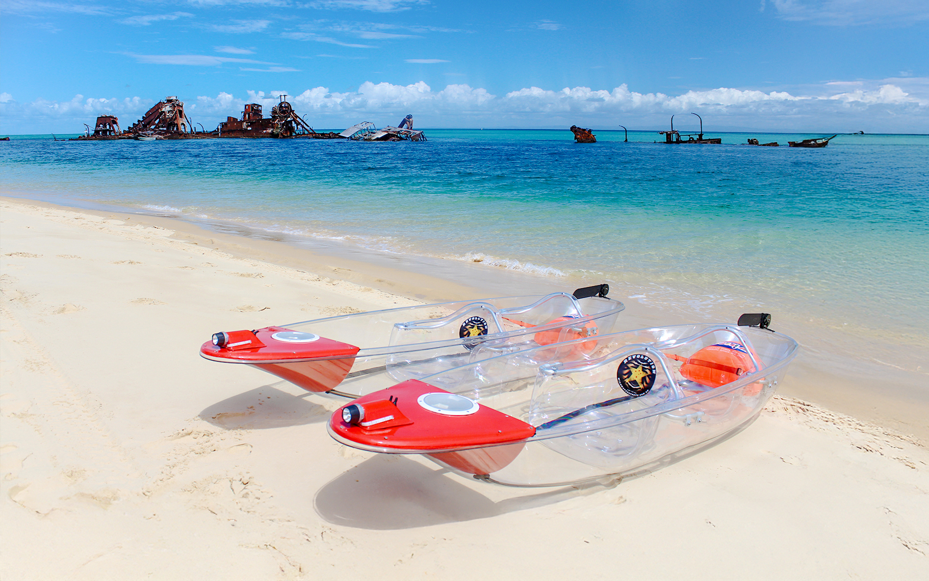 Clear kayaks on Moreton Island beach with shipwrecks in the background.