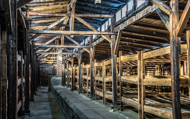 Wooden barracks interior with rows of bunk beds and exposed beams.