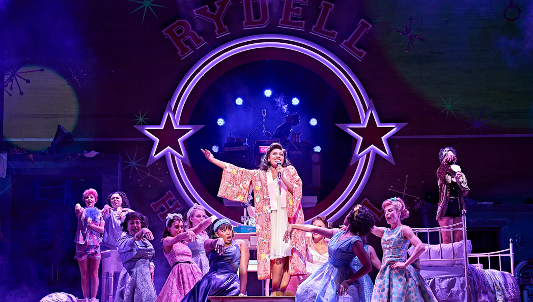 Cast performing a musical number on stage at Rydell High in the Grease production.