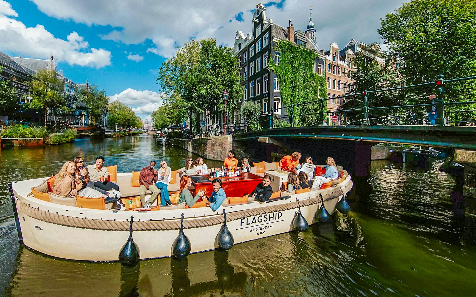 Luxury open boat cruise on Amsterdam's canals with passengers enjoying drinks.