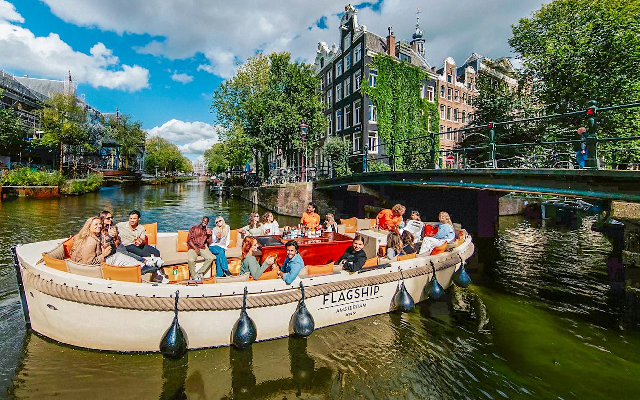 Luxury open boat cruise on Amsterdam's canals with passengers enjoying drinks.
