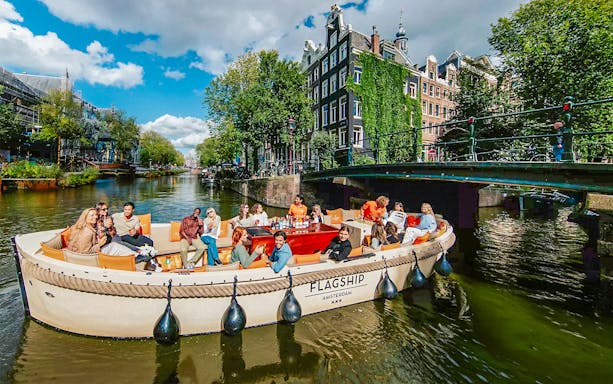 Luxury open boat cruise on Amsterdam canal with passengers enjoying drinks.