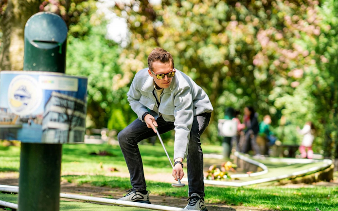 Man playing mini-golf at Midgetgolf Parkhaven, surrounded by greenery.