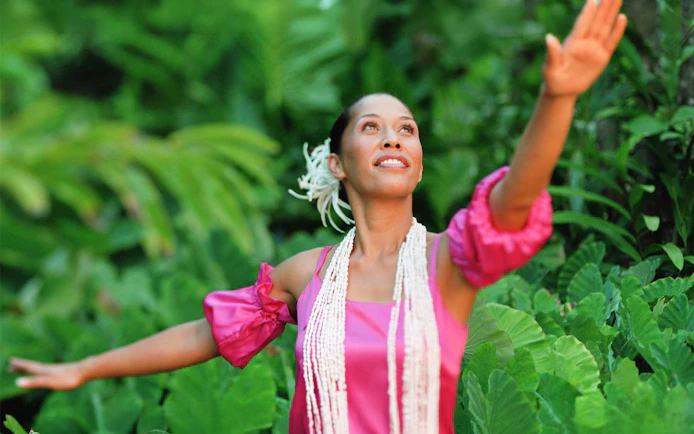 Performer in traditional attire at Smiths Family Garden Luau, surrounded by lush greenery.