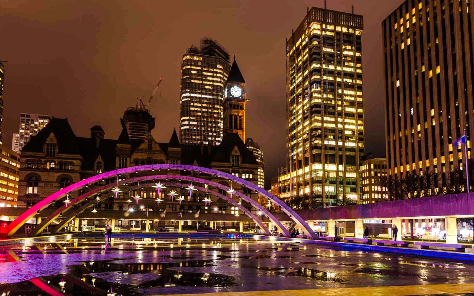 Nathan Phillips Square at night with illuminated arches and city skyline in Toronto.