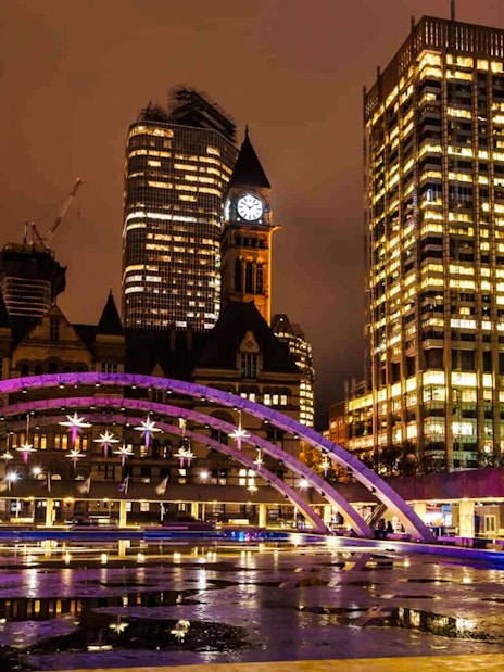 Nathan Phillips Square at night with illuminated arches and city skyline in Toronto.