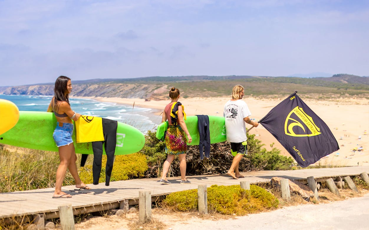 Surfers carrying boards and a flag at Carrapateira Beach, Portugal.