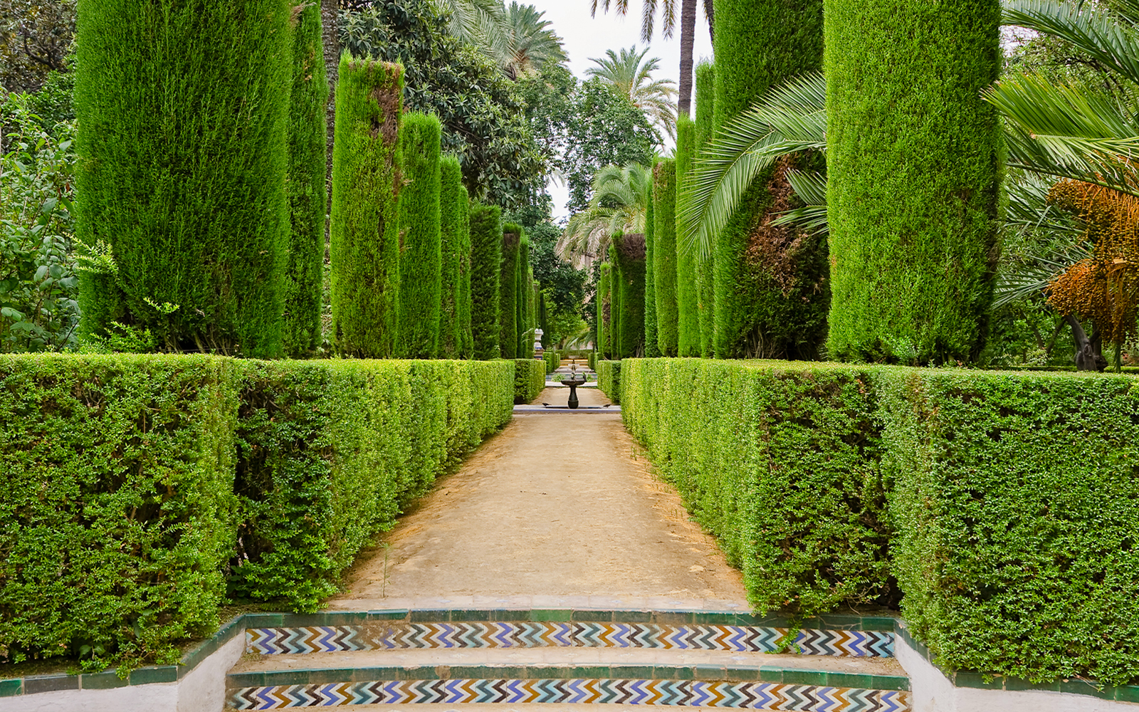 Garden of the Poets courtyard with lush greenery and intricate arches, Alcazar Palace, Seville.