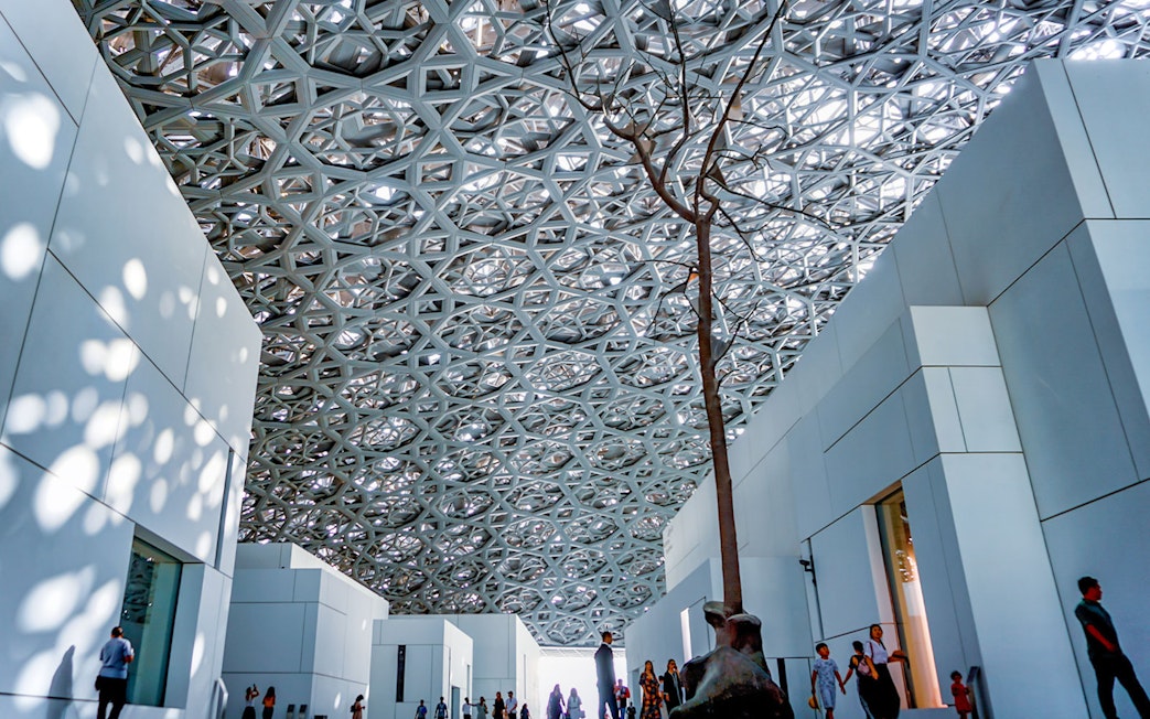 Rain of Light Dome at Louvre Museum Abu Dhabi with visitors walking below.
