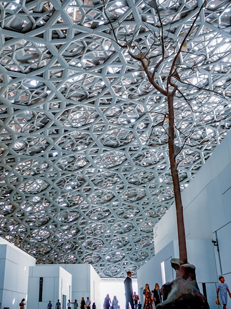 Rain of Light Dome at Louvre Museum Abu Dhabi with visitors walking below.