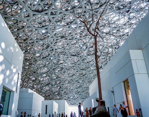 Rain of Light Dome at Louvre Museum Abu Dhabi with visitors walking below.