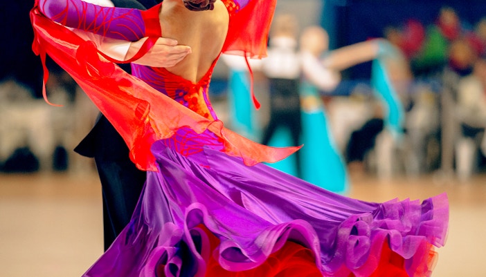 Casal dançando valsa em um grande salão de baile, exibindo movimentos de dança elegantes.