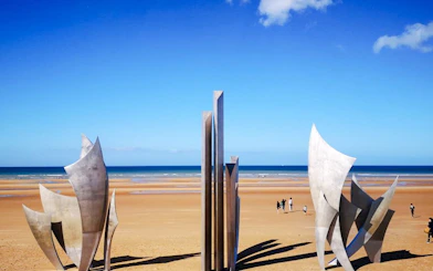 Les Braves sculpture on Omaha Beach, Normandy, France with ocean backdrop.