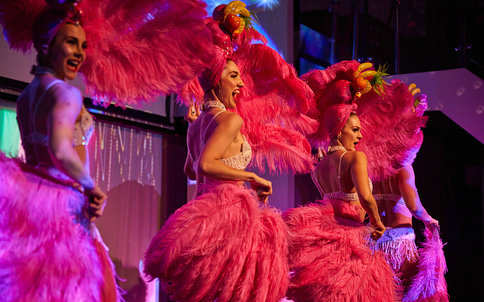 Cabaret performers in vibrant costumes on a cruise stage.