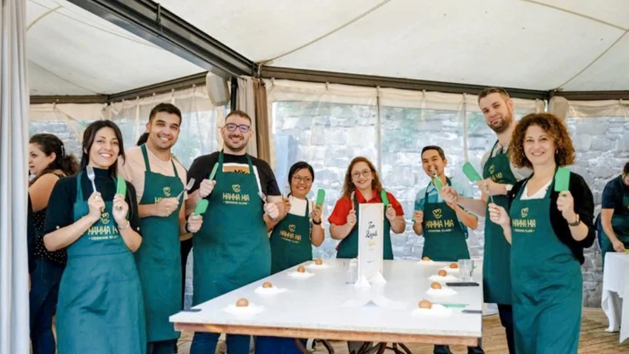 Group of people in aprons holding utensils during a cooking class in Rome.