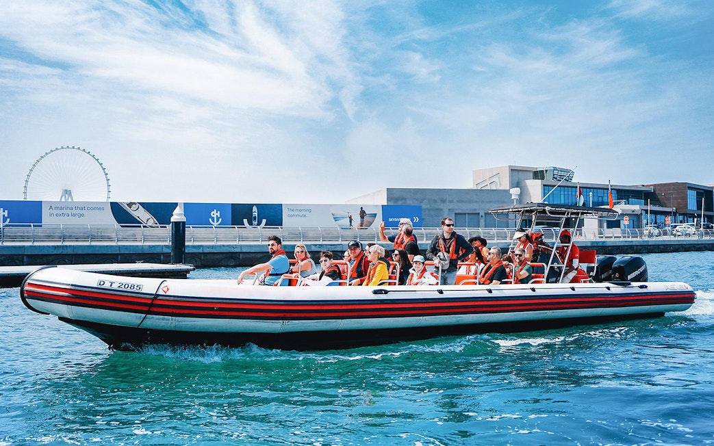 Speedboat with tourists on Dubai Marina tour, passing by waterfront attractions.