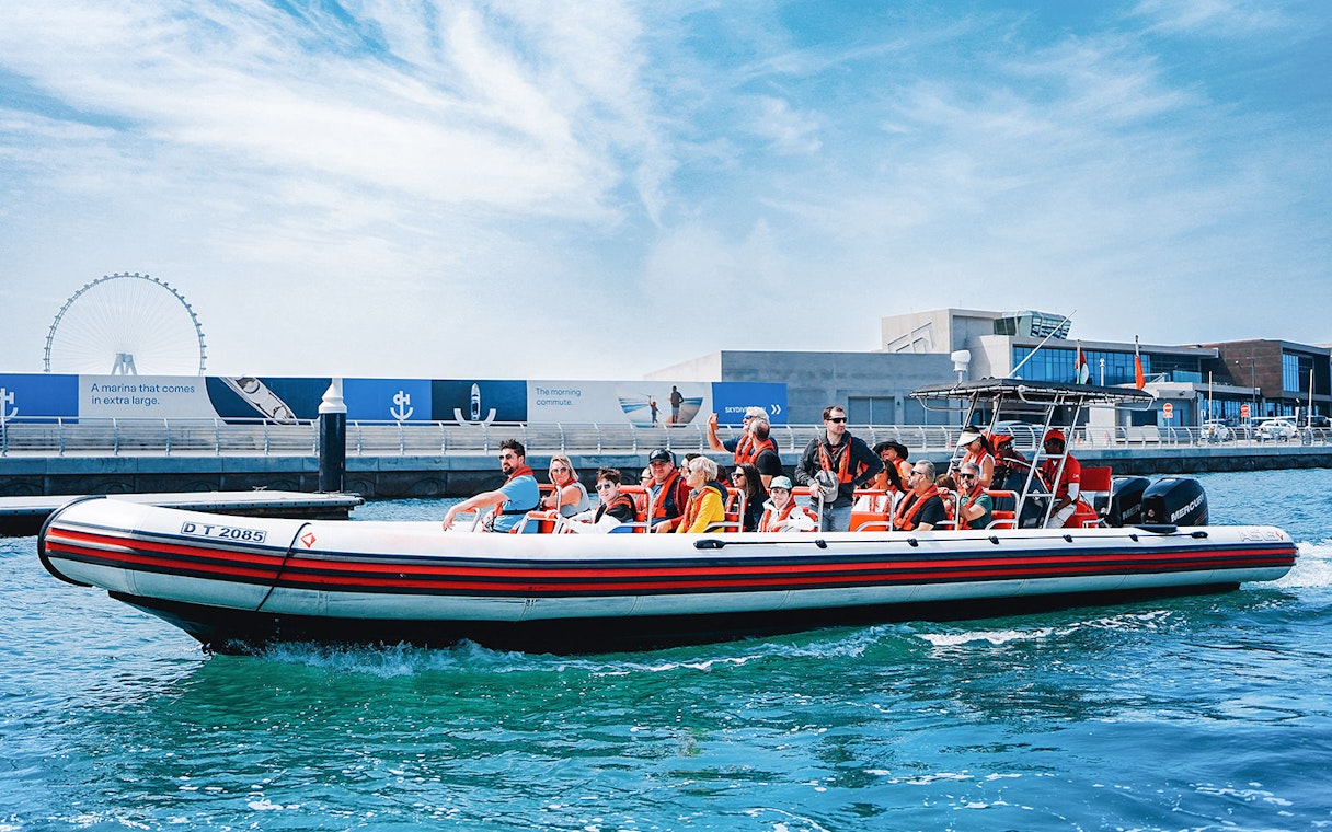 Speedboat with tourists on Dubai Marina tour, passing by waterfront attractions.