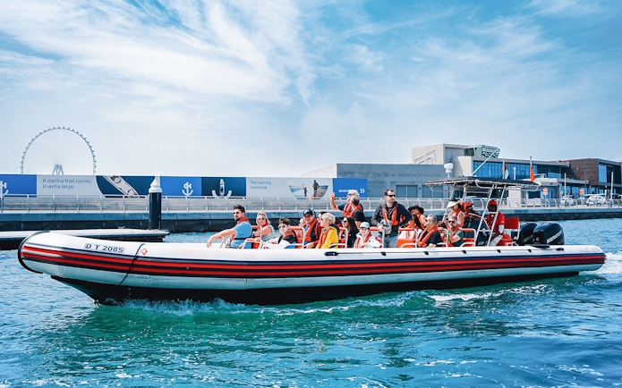 Speedboat with tourists on Dubai Marina tour, passing by waterfront attractions.