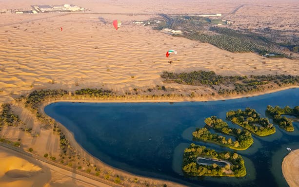 Paramotor flying over desert dunes and oasis in Dubai.