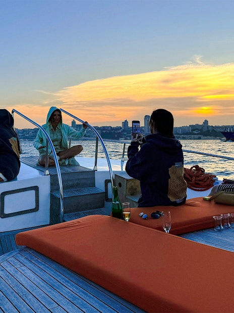 Visitors relaxing on a private luxury yacht at sunset, city skyline in the background.