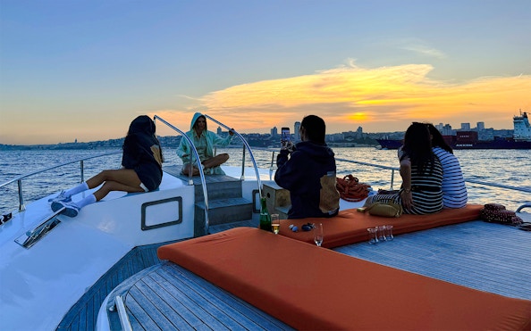 Visitors relaxing on a private luxury yacht at sunset, city skyline in the background.
