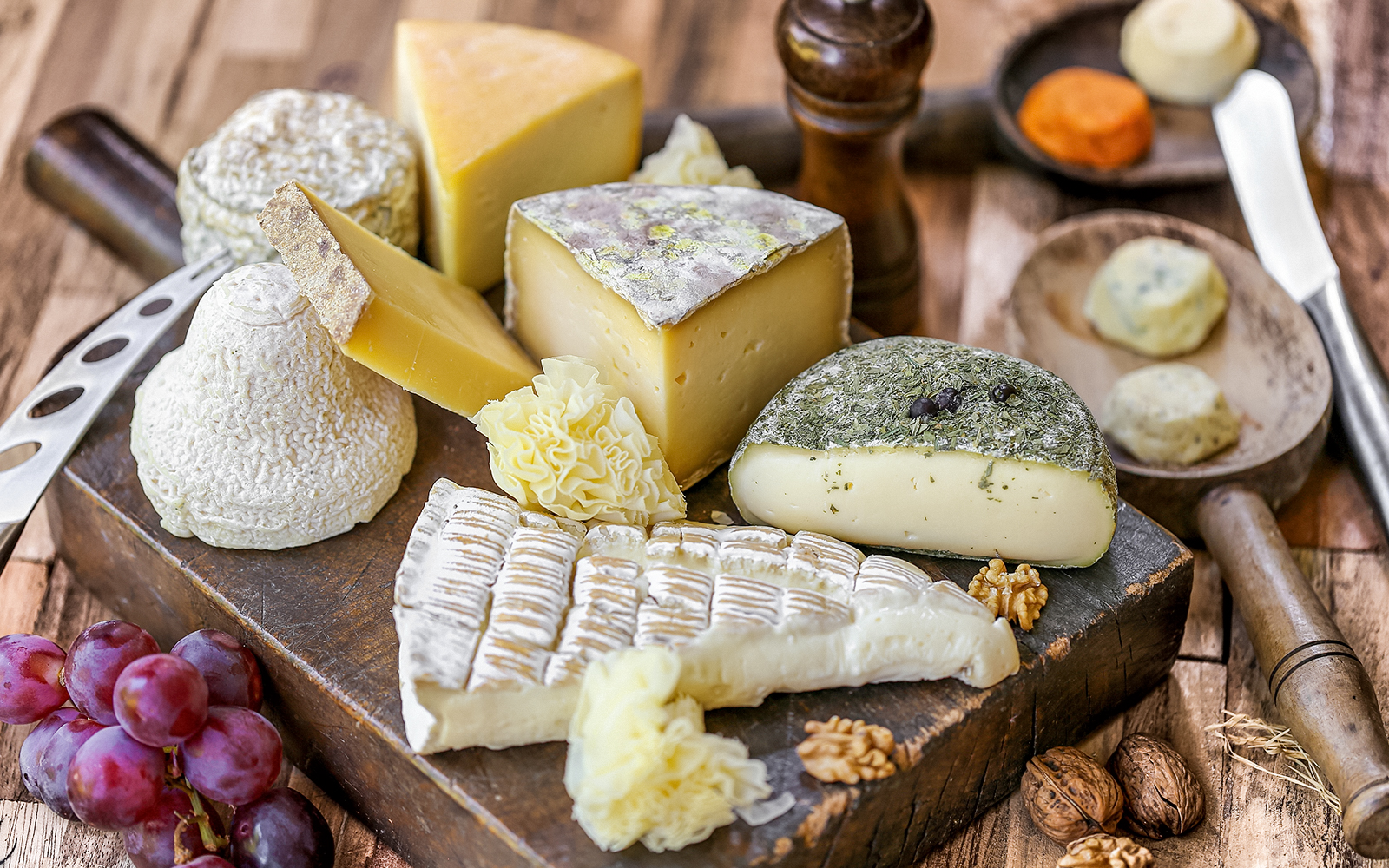 Assorted French cheeses and grapes on a wooden board, featured in Paris Saint Germain food tours.