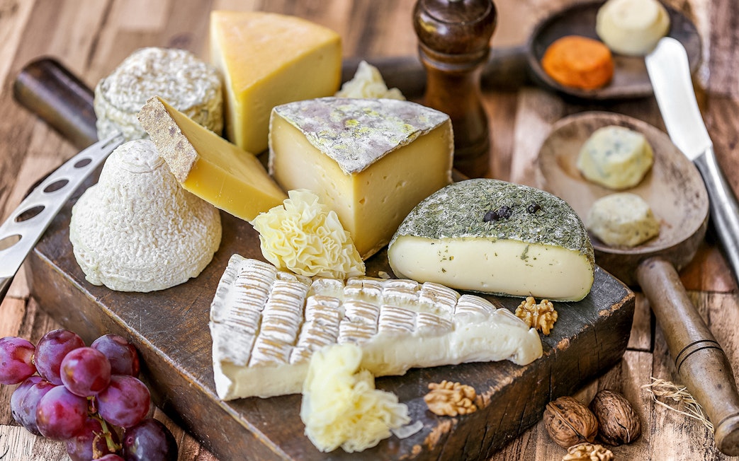 Assorted French cheeses and grapes on a wooden board, featured in Paris Saint Germain food tours.