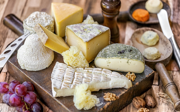Assorted French cheeses and grapes on a wooden board, featured in Paris Saint Germain food tours.