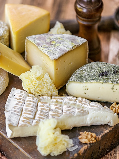 Assorted French cheeses and grapes on a wooden board, featured in Paris Saint Germain food tours.