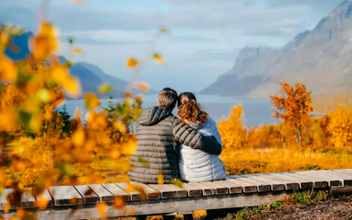 Couple sitting on a bench overlooking Sommarøy Fjord with autumn foliage, Tromsø.