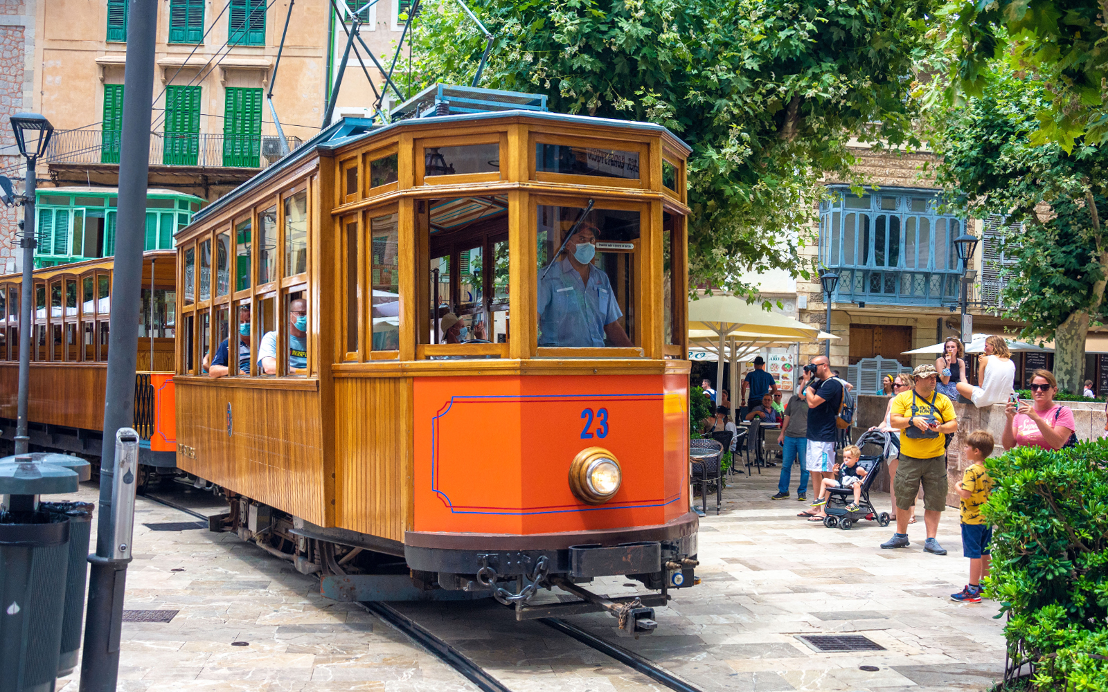 Historic tram in Soller, Mallorca, with passengers and tourists nearby.