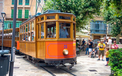 Historic tram in Soller, Mallorca, with passengers and tourists nearby.