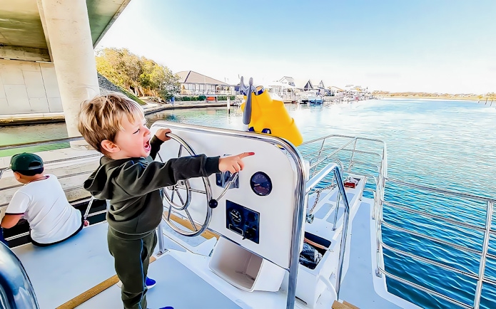 Child steering a boat, pointing towards dolphins in the water.