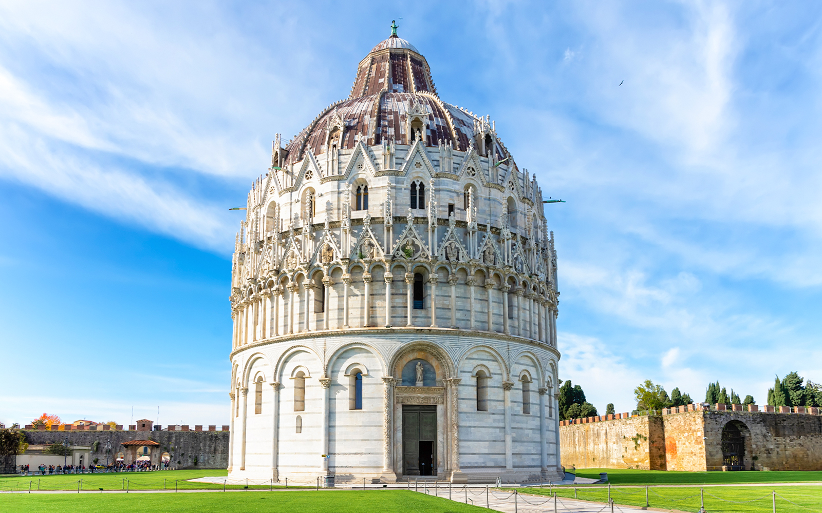 Pisa Baptistery with guided tour group in foreground, Leaning Tower visible in background.