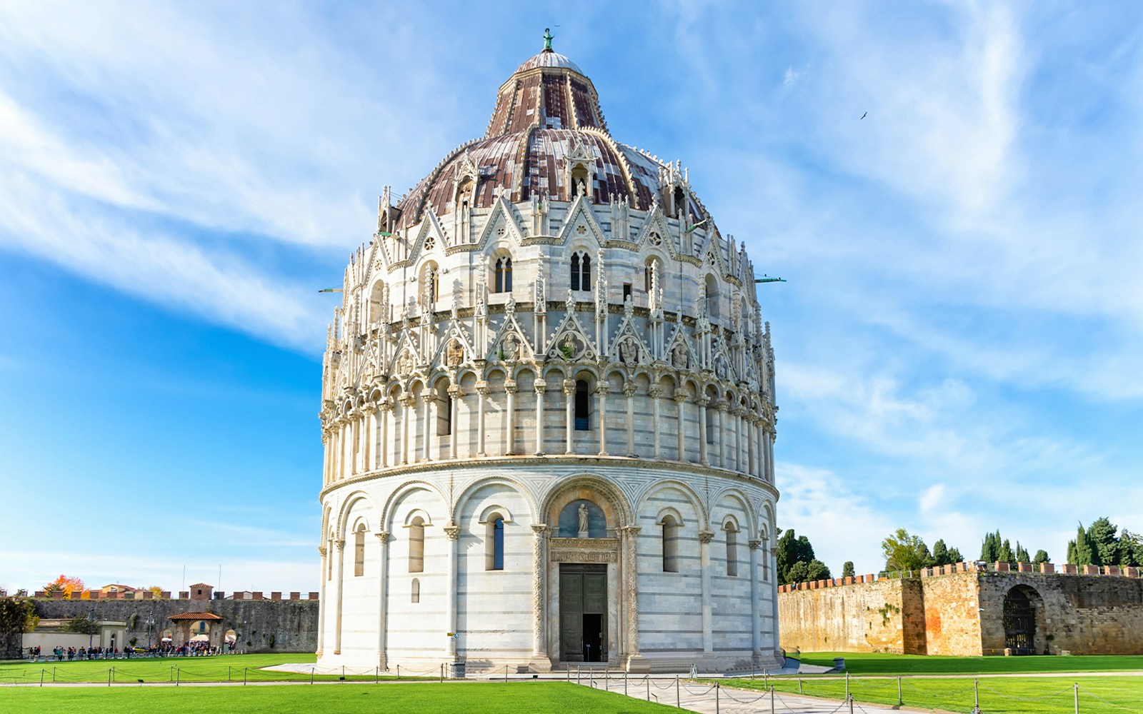 Guided tour group in front of Pisa Baptistery and Leaning Tower, Italy.