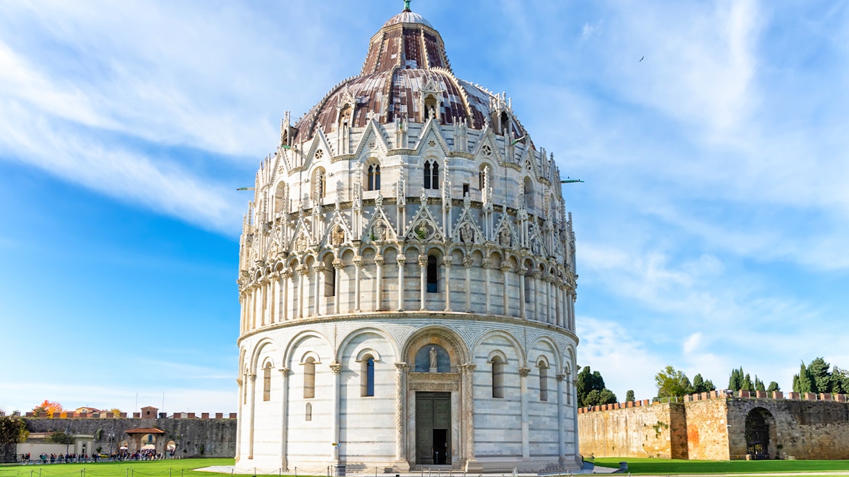Guided tour group in front of Pisa Baptistery and Leaning Tower, Italy.