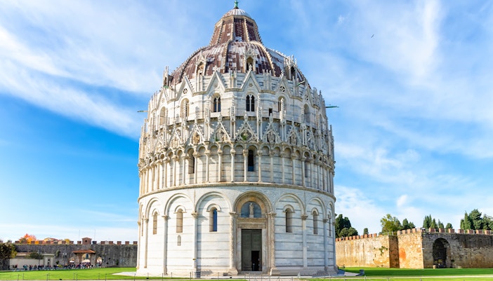 Guided tour group in front of Pisa Baptistery and Leaning Tower, Italy.