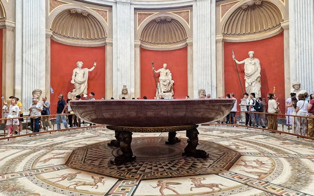 Sala Rotonda at the Vatican Museums featuring ancient Roman sculptures and a large red porphyry basin.