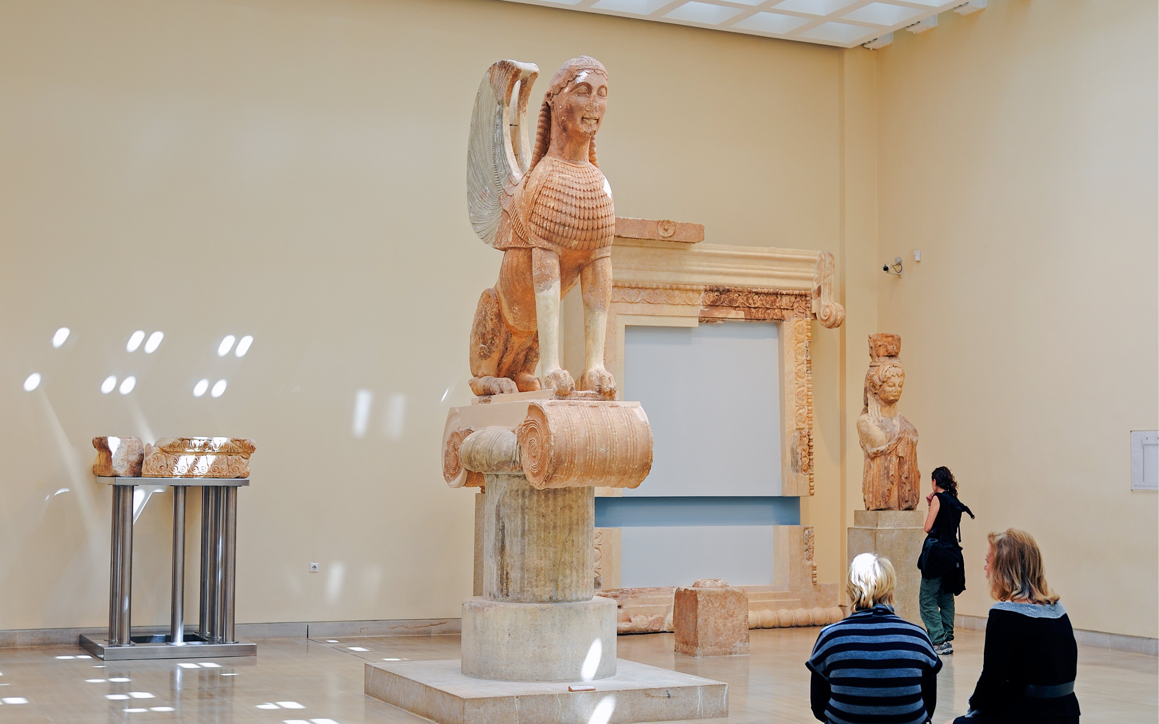 Sphinx of Naxos statue in Delphi museum, Greece, with visitors observing.