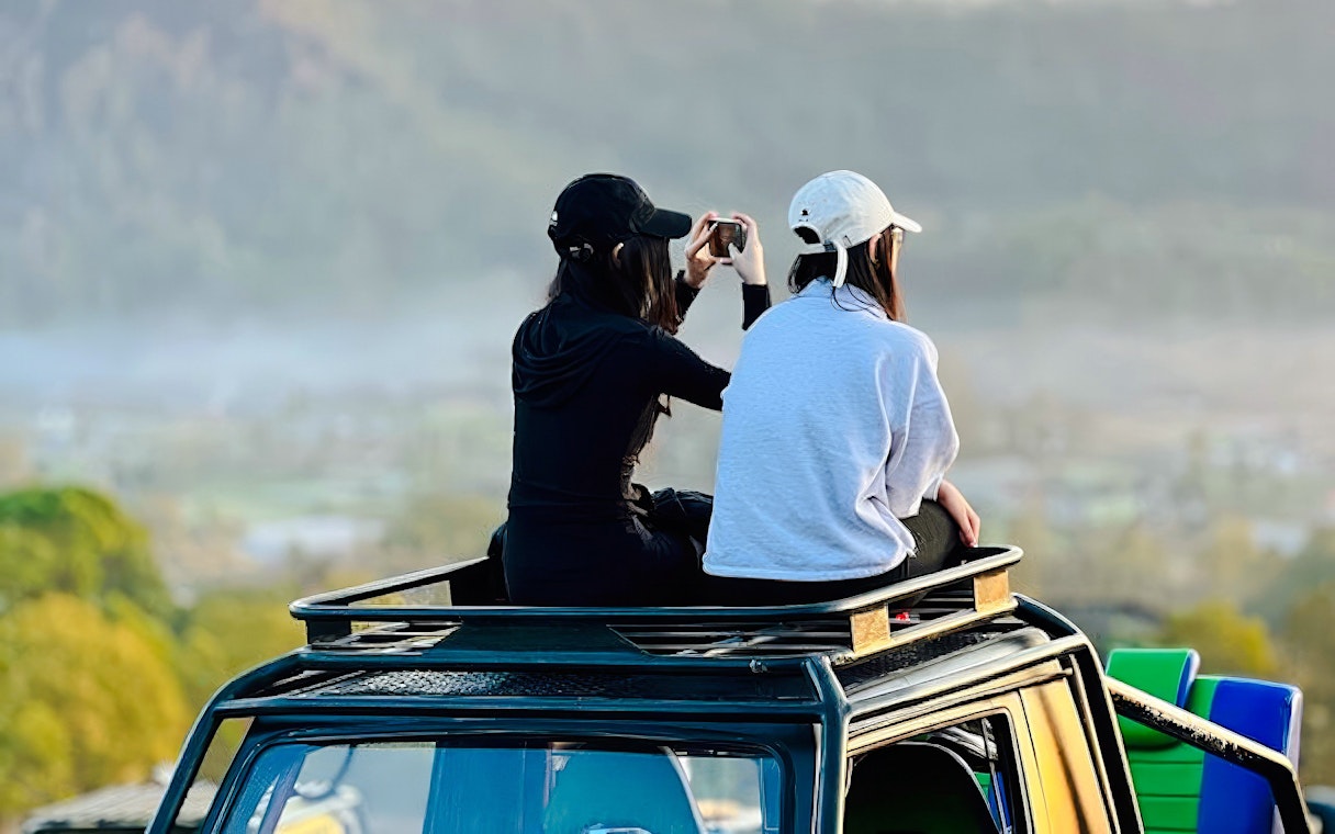 Two people sitting on a vehicle roof, capturing the view during Black Lava Exploration in Bali.