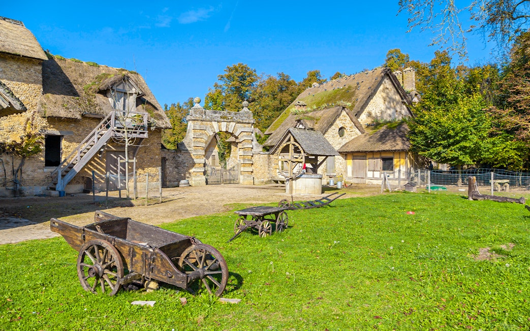 Rustic village scene at Marie-Antoinette's Domain, Versailles, with stone cottages and wooden carts.